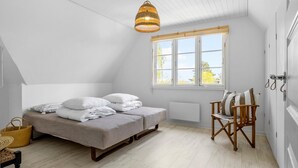 Een slaapkamer met een bed, een stoel, een raam en een hanglamp.