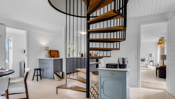 Een moderne keuken met een centrale spiraaltrap, een eethoek met een houten tafel en stoelen, en een lichtblauwe kast.
