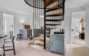 Una cuina moderna amb una escala espiraltra central, una zona de menjador amb taula i cadires de fusta, i un armari blau cel.
