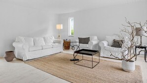 Een minimalistische woonkamer met een witte bank, een bijzettafeltje en een potplant.