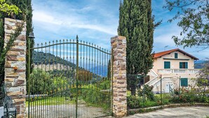 Une propriétéClose, entourée d’un mur de pierre, dotée d’un portail en métal et abritant une maison avec un toit rouge et des volets verts.