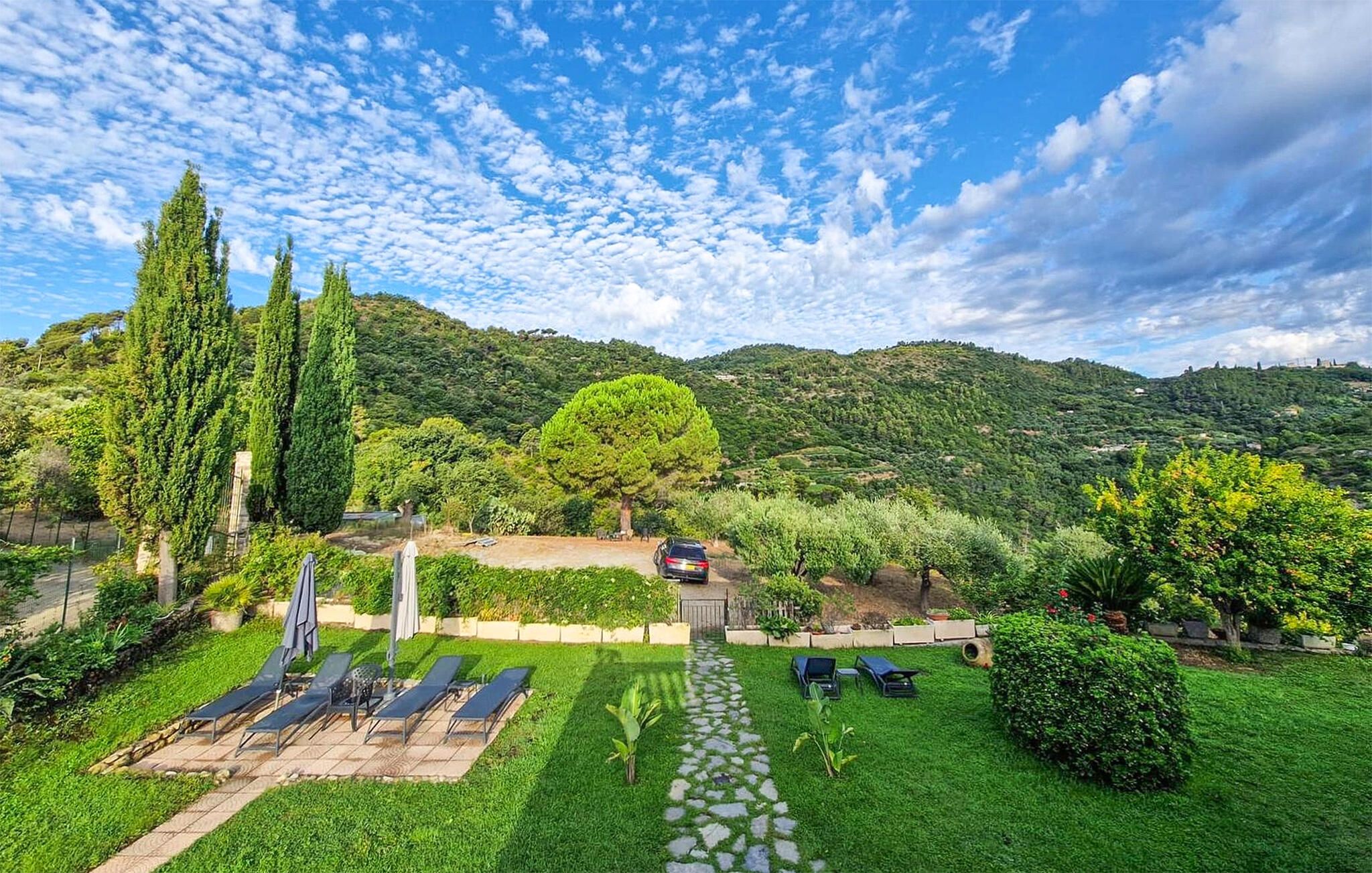 A garden with a stone pathway leading to a seating area with sun loungers.