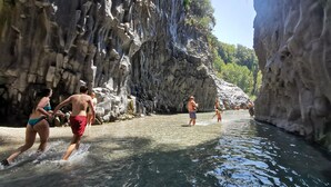 Un groupe de personnes traverse à gué un cours d’eau étroit et rocheux, bordé de falaises abruptes.