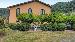 Un bâtiment à deux étages, doté d’une façade jaune, de trois fenêtres en arc de cercle et d’un petit patio aménagé avec des sièges extérieurs.