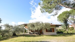 Una casa de un piso con techo de tejas, rodeada de olivos y un césped.