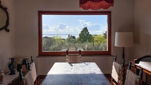 Una habitación con un ventanal grande, una mesa, sillas, una lámpara y un espejo decorativo.