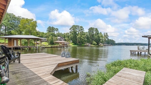 Un muelle de madera que se adentra en un lago, con un pabellón y una zona de estar cubierta.