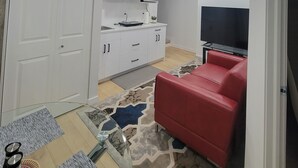 Ett kompakt bostadsutrymme med ett litet kök, en röd soffa och en platt-TV.