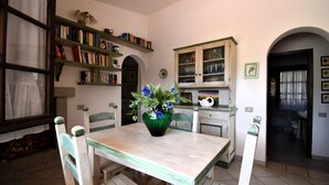 Et spiseområde med et træbord, stole, en vase med blomster, en reol og et køkken med skabe og vask.