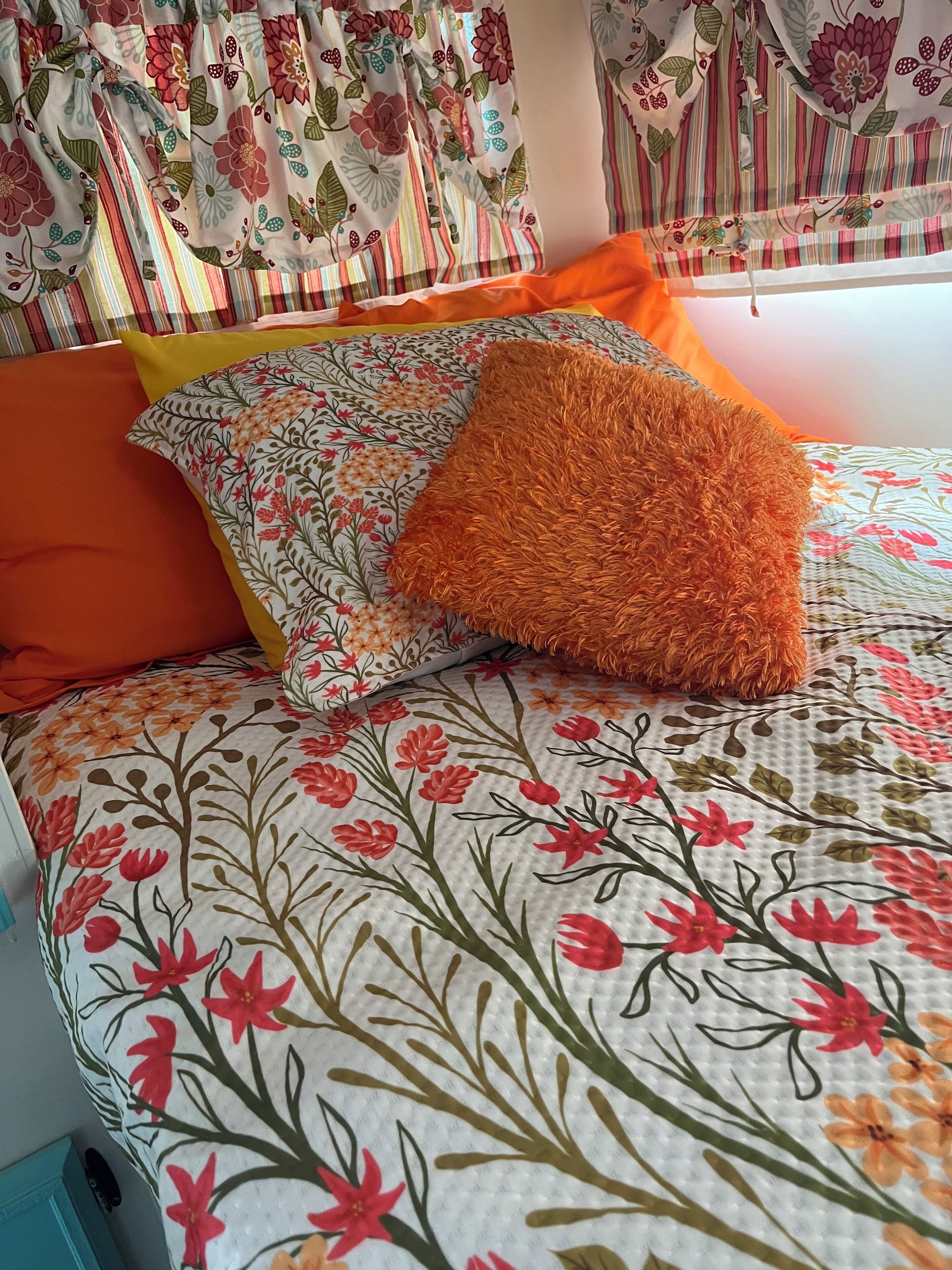 A bed with floral bedding, orange pillows, and striped curtains.