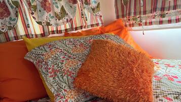 A bed with floral bedding, orange pillows, and striped curtains.