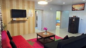 Un salon moderne avec un canapé rouge, un canapé noir, un meuble TV en bois, une petite table avec un vase et un réfrigérateur.