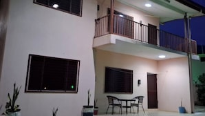 Un bâtiment à deux étages doté d’un balcon, de grandes fenêtres et d’un petit espace patio avec une table et des chaises.
