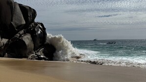 Ein Strand mit einem Felsen und brechenden Wellen.