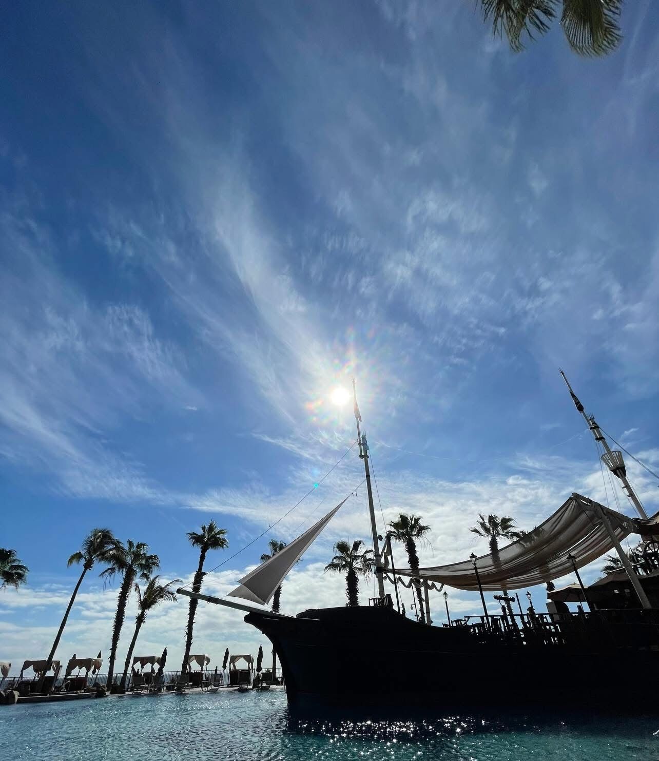 A large boat docked at a marina with palm trees in the background and a clear sky.