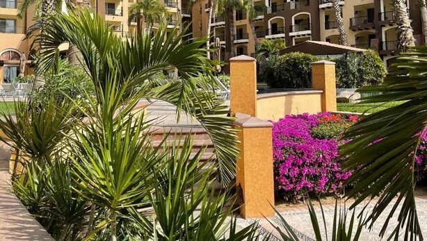 Ein Hotel mit mehreren Etagen, Balkonen und einem Innenhof mit Palmen und Blumen.