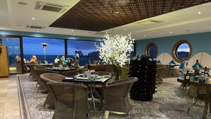 Ein Restaurant mit Korbmöbeln, einem Ziertee und Blick aufs Meer.