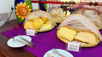 Une table avec des paniers étiquetés « Pão de Sal » et « Pão de Milho », des ustensiles et un vase décoratif contenant des tournesols.