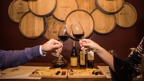 A wine tasting event with wooden barrels in the background, a bottle of wine, and a cheese board on the table.