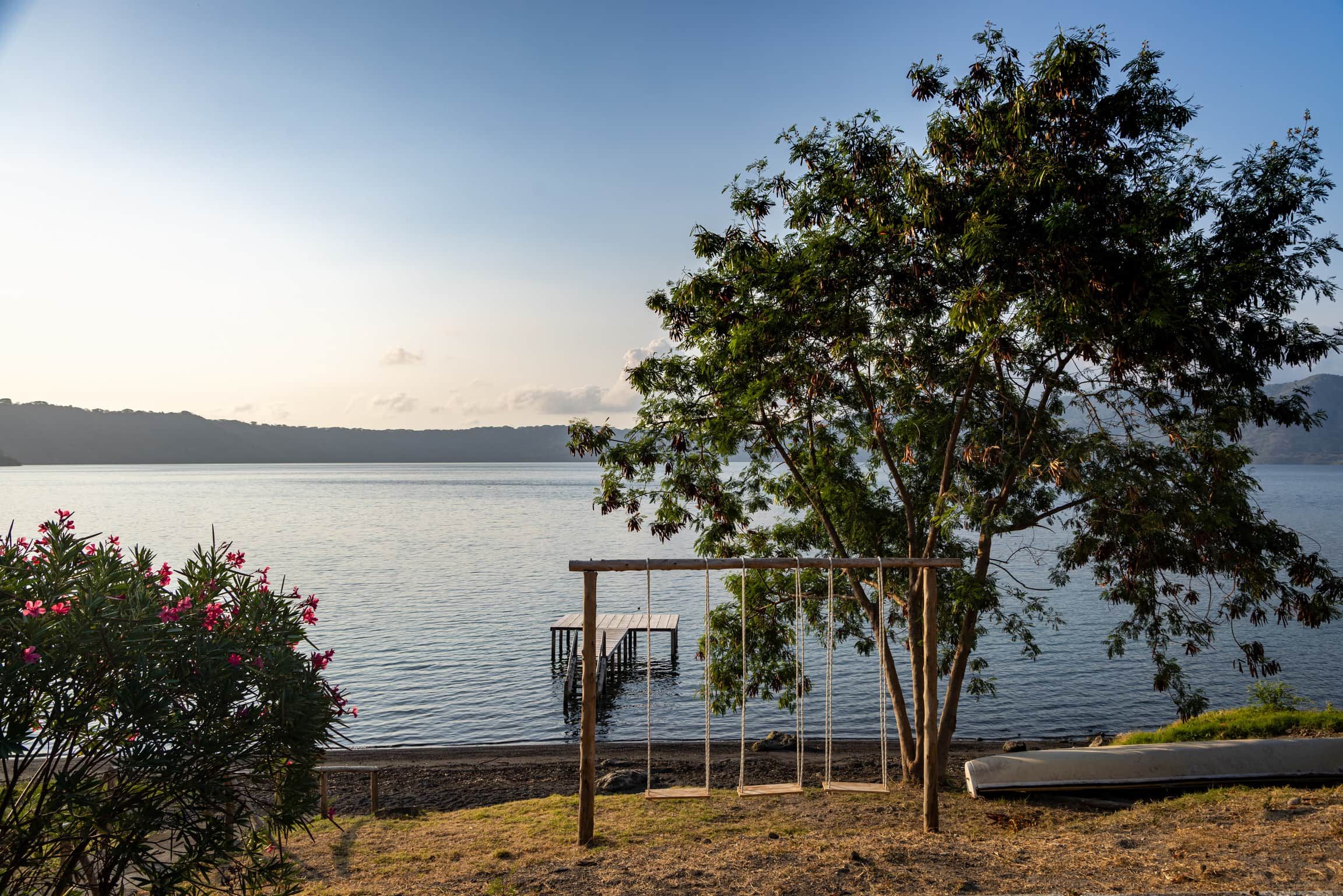 A lakeside view with a wooden swing set, a boat, and a clear sky.
