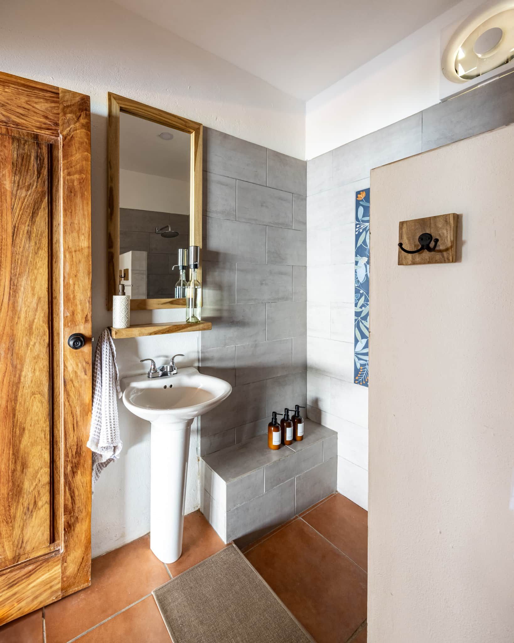 A bathroom with a wooden door, a white sink, a mirror, and a shelf with toiletries.