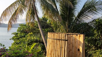 A bamboo gate leading to a beach area with palm trees and purple flowers.