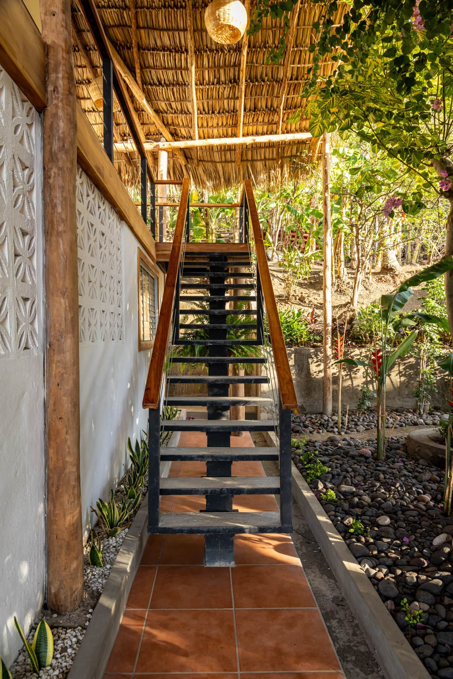 A staircase leading to a covered area with a thatched roof, surrounded by greenery and a garden.