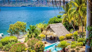Un resort tropical con piscina, construcción de techo de paja y exuberante follaje.
