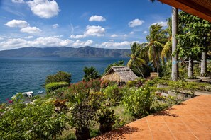 Un paysage tropical avec une hutte au toit de chaume, des palmiers et une vue sur une vaste étendue d’eau.