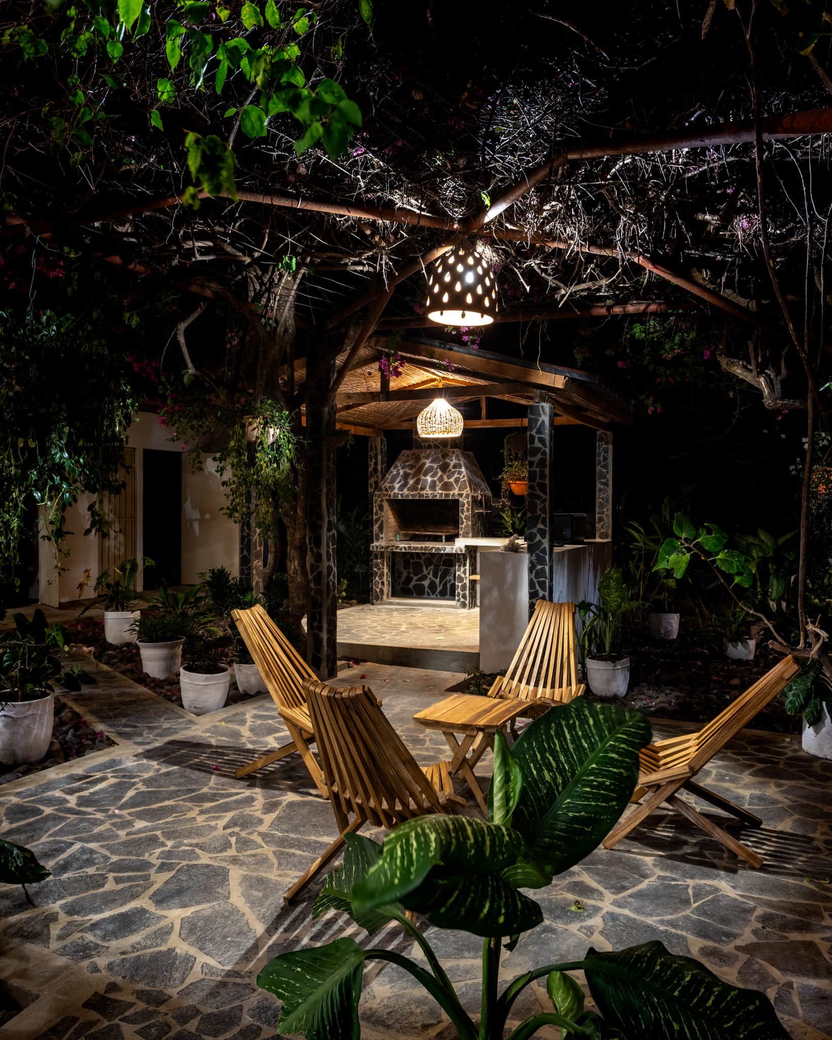 An outdoor patio with stone flooring, wooden furniture, and a stone-built barbecue area.