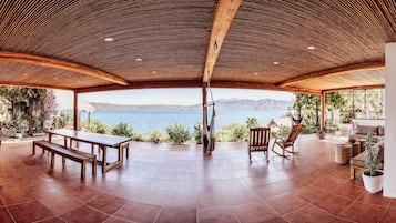 Een ruim terras met uitzicht op zee, houten meubels en potten met planten.