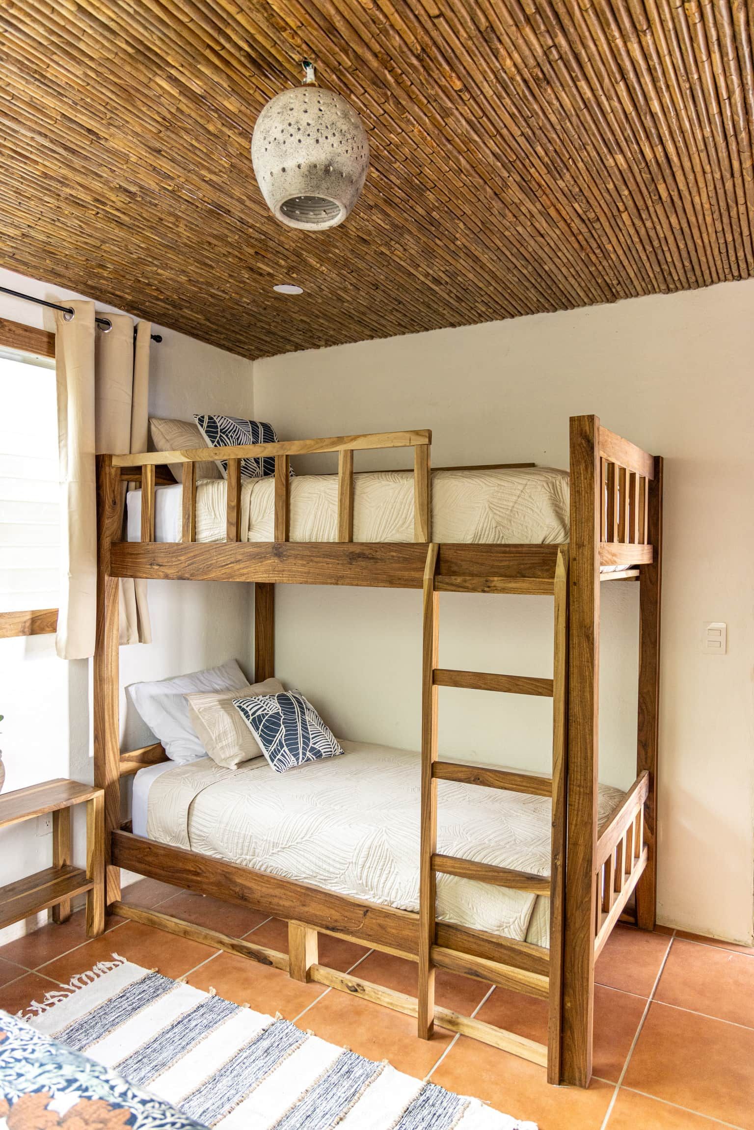 A bunk bed with a wooden frame, a ceiling with a woven pattern, and a small table with a cushion.