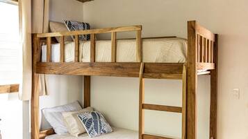 A bunk bed with a wooden frame, a ceiling with a woven pattern, and a small table with a cushion.