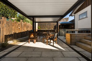 A covered patio with a fire pit, outdoor seating, and a stone fireplace. - Alp Studios | 2-Bedroom Luxury Apartment, Sleeps 5, Mountain Views, Private Balconies & Shared Spa (Wānaka)