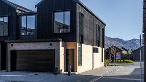 Una casa moderna de dos pisos con garaje, ventanas amplias y vista a las montañas.