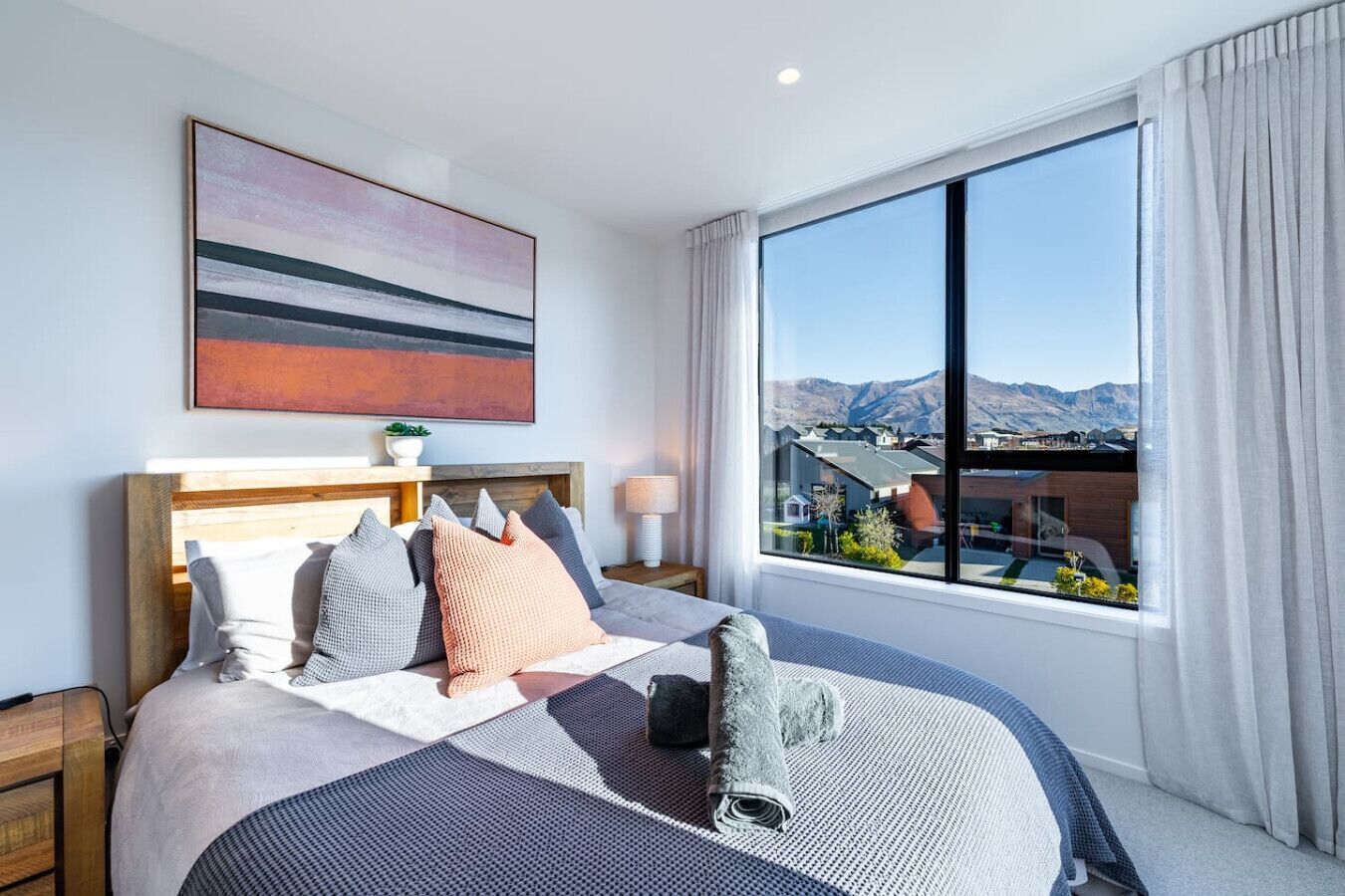 Ein modernes Hotelzimmer mit einem großen Bett, Blick auf Berge und Stadtlandschaft durch das Fenster.