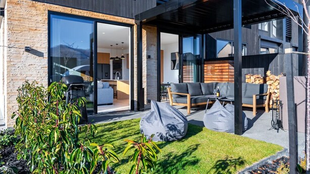 Una casa moderna con puerta de cristal que da a una cocina y sala de estar, un área de estar cubierta al aire libre y un césped bien cuidado.