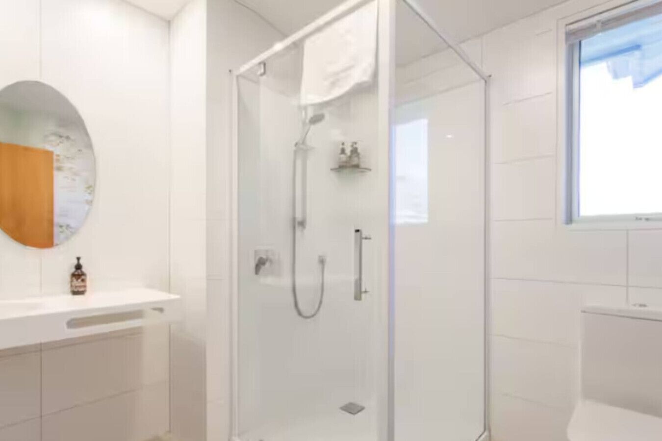 Un baño moderno con ducha de vidrio, tocador blanco y espejo redondo.