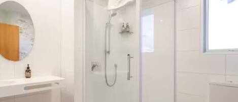 Un baño moderno con ducha de vidrio, tocador blanco y espejo redondo.