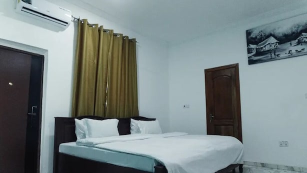Un dormitorio con cama, cortinas, una puerta y aire acondicionado de pared.