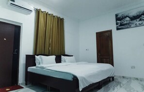 A bedroom with a bed, curtains, a door, and a wall-mounted air conditioner. - RAGANT HOTEL (Cape Coast)