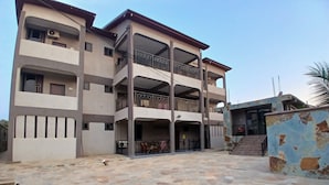 Un edificio de varios pisos con balcones, una entrada cubierta y un patio empedrado de piedra.