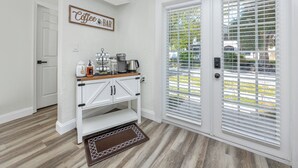 A kitchen with a coffee bar, white cabinetry, and a view through the door. - Charming 3BR retreat w/ Private yard- 15 min to Gulf Beaches & 6 min to DTSP (St. Petersburg)