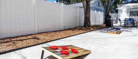 Un patio con una mesa de madera, cojines rojos y una parrilla.