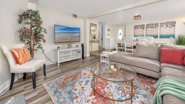 A living room with a sofa, armchair, coffee table, and a large painting. - Charming 3BR retreat w/ Private yard- 15 min to Gulf Beaches & 6 min to DTSP (St. Petersburg)