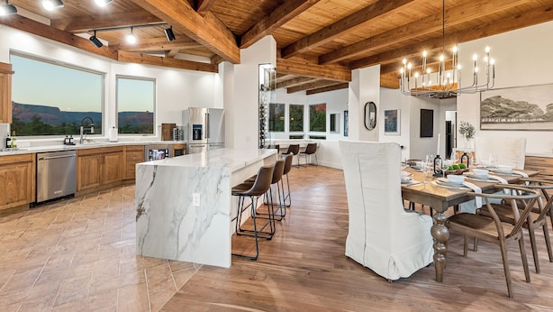 A spacious kitchen with a marble island, wooden beams, and large windows offering a view of the landscape. - The Belvedere // Hot Tub, Sauna & Red Rock Views (Sedona)