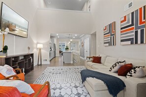 A modern living room with a sofa, a coffee table, and a TV. There is a kitchen area in the background.