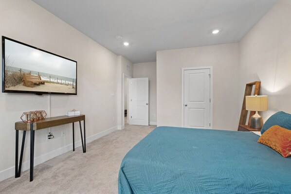 A bedroom with a bed, a TV on the wall, a desk, and a door.