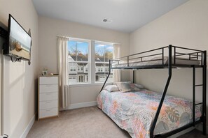 Een slaapkamer met een stapelbed, een dressoir, een raam met gordijnen en een schilderij aan de muur.