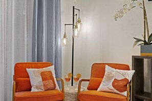 Une pièce comprenant deux fauteuils orange à revêtement en tissu, dotés de coussins à motifs, un grand lampadaire avec plusieurs sources de lumière et une plante orchidée en pot.